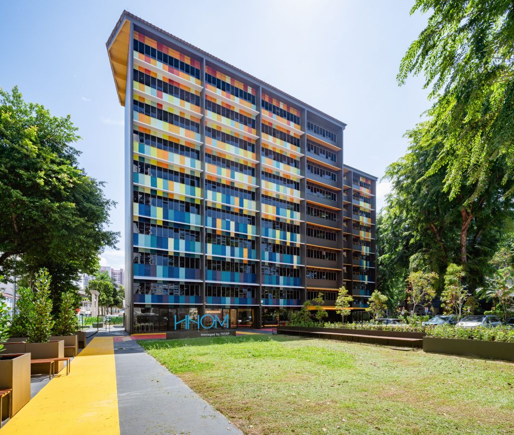 The ground-level entrance of the HHOM Nurse Hostel, featuring a brightly painted red and yellow drop-off area.