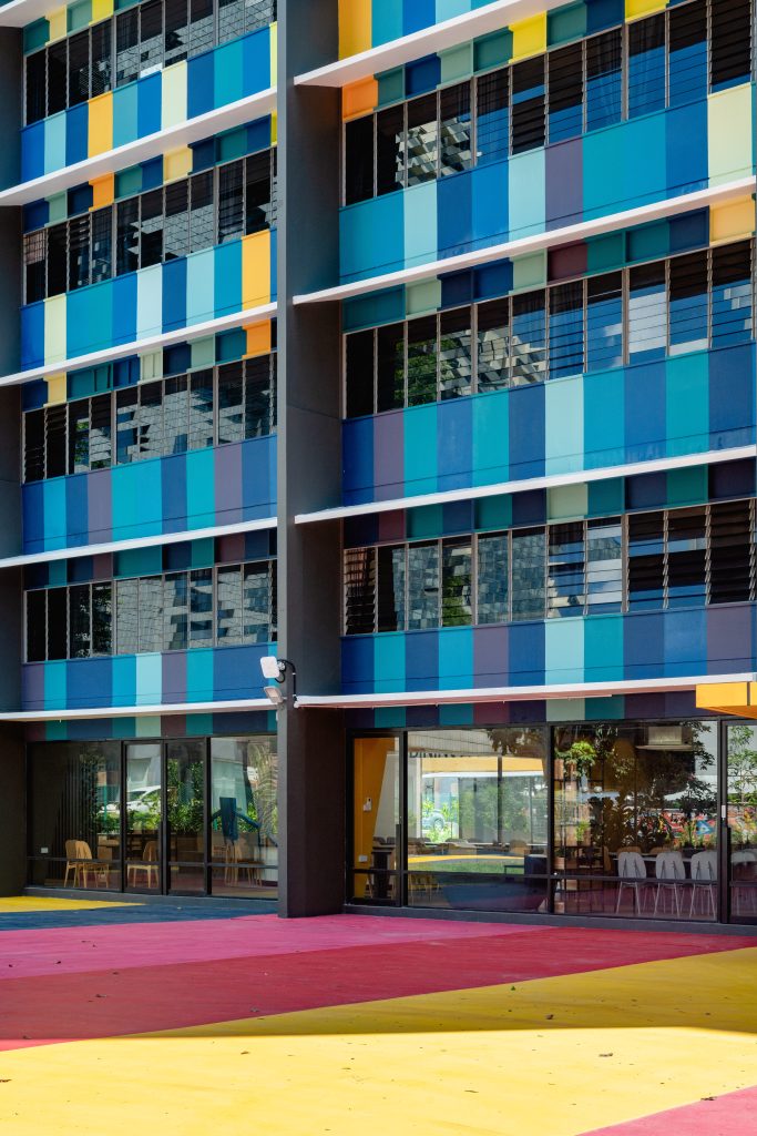 A ground-level view of the HHOM Nurse Hostel, showing the colourful facade meeting the painted red and yellow pavement.