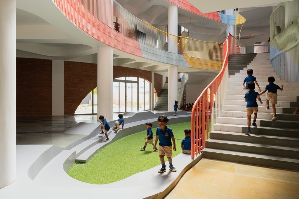 A colourful central school courtyard featuring green artificial grass and sweeping multi-level staircases.