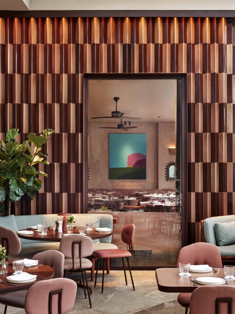An intimate dining nook featuring dusty rose walls, warm lighting, and a vibrant landscape painting.
