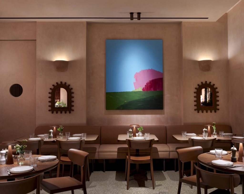 A detailed view of a dining corner featuring textured pink walls adorned with small, colourful art pieces.