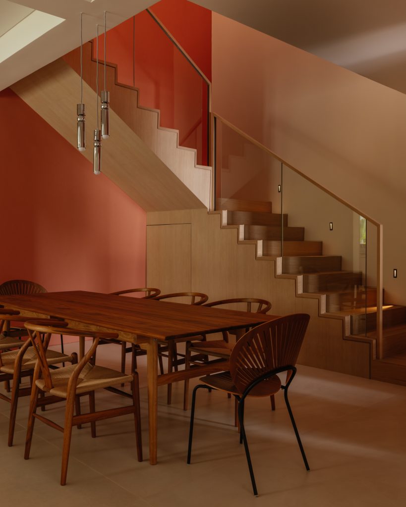 A wooden dining table and chairs positioned beneath a striking orange stairwell.