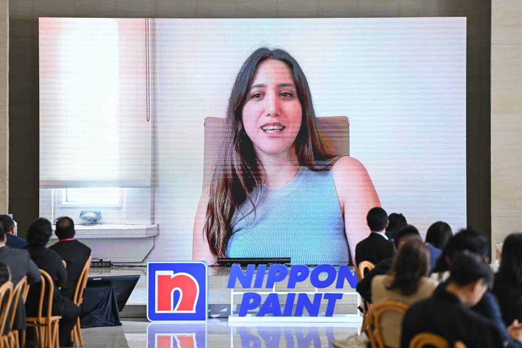 A female representative from KONTRA giving her acceptance speech via a large digital screen on stage.