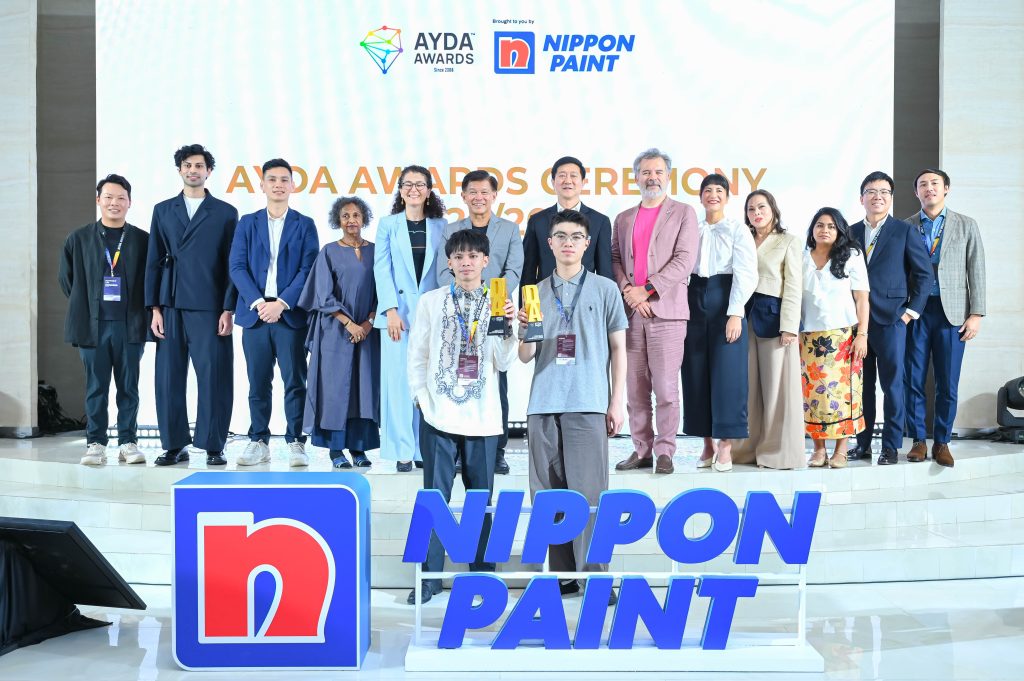 Designers of the Year Ejhey Durias and Jackie Jiang Haoran proudly holding their golden trophies on stage with the judges.