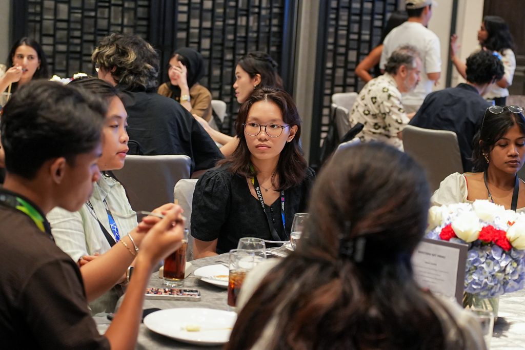 A young female designer listening intently while seated at a dining table with peers.