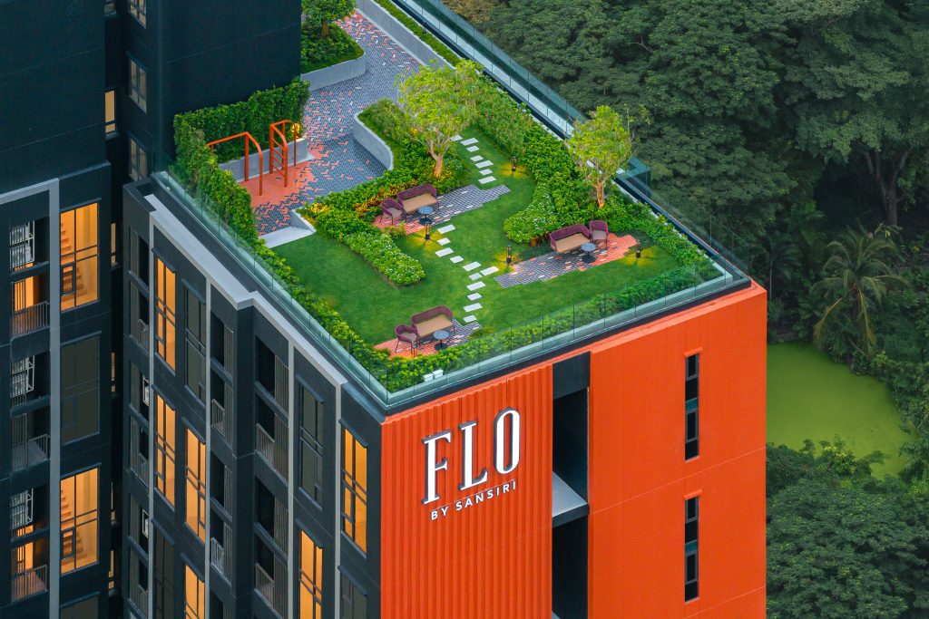 A mid-level roof garden on the Flo building, featuring lush greenery against the striking orange and black facade.