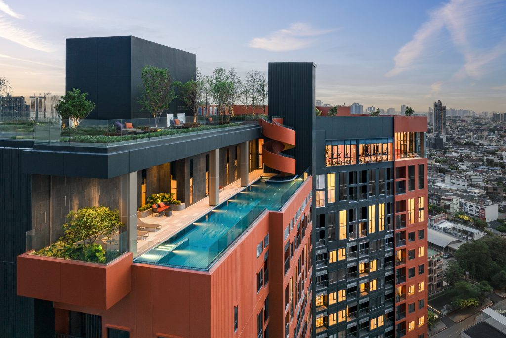 A tall residential building painted in striking orange and black, standing out against the Bangkok skyline.