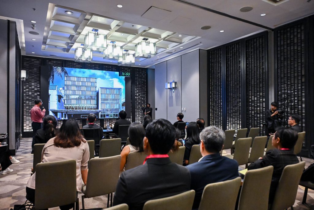 An audience seated in a presentation room watching a digital architectural render on a large screen.