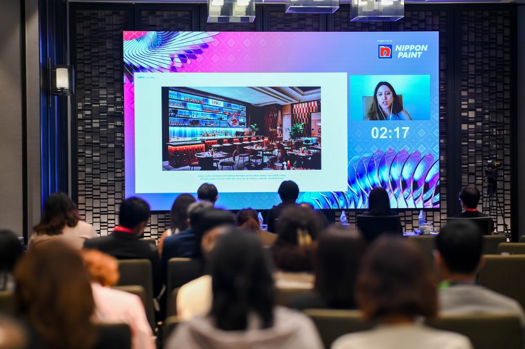 A large screen displaying a virtual presentation by a female designer alongside her project, Epoca.
