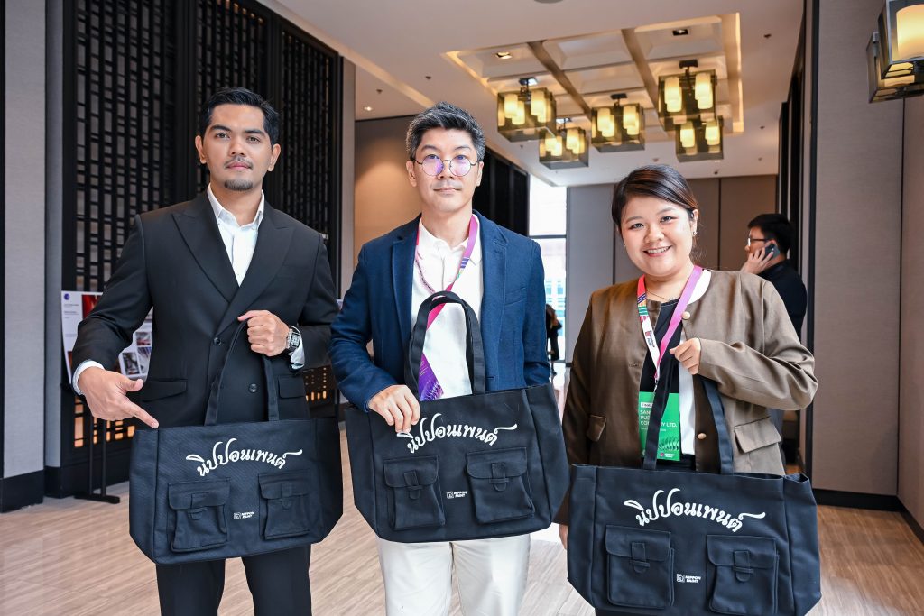 Three smiling attendees proudly holding their black canvas Nippon Paint goodie bags in the lobby.