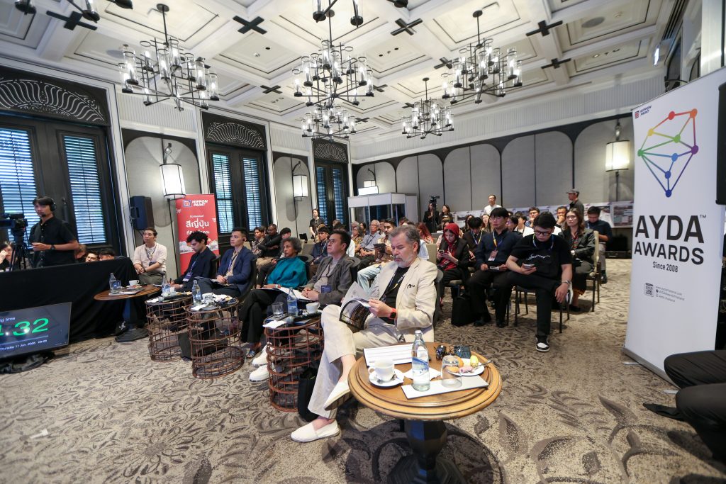 Wide shot of the international judging panel seated in a grand hall, reviewing presentation materials.