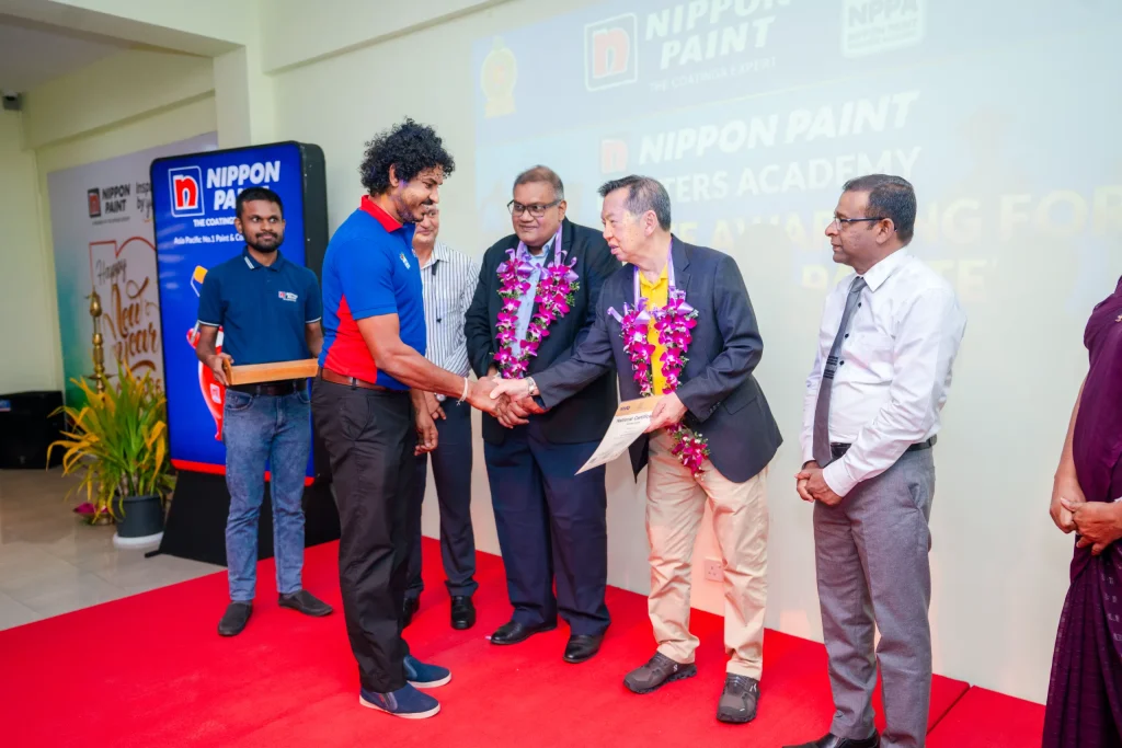 A professional painter receives a certificate on stage from executives wearing floral garlands.