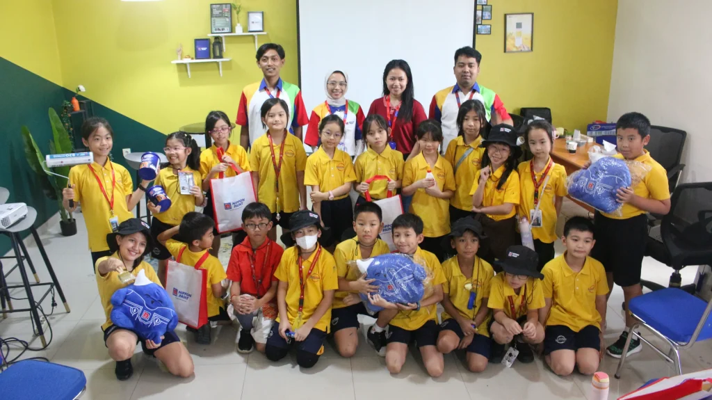 Smiling children hold painting supplies and corporate merchandise alongside adult instructors.