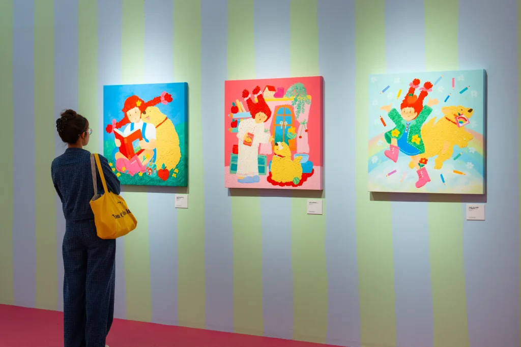 A visitor admires three bright, cheerful paintings of a girl and her yellow dog.