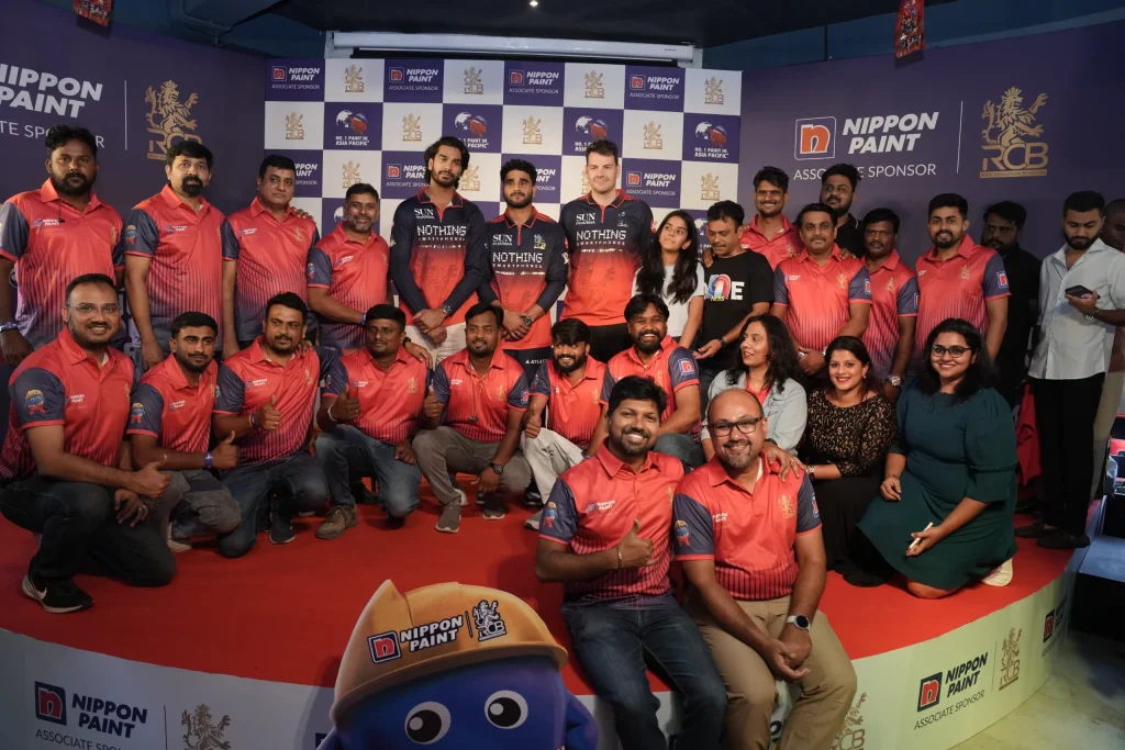 RCB cricket players posing for a large group photo with enthusiastic staff and partners.
