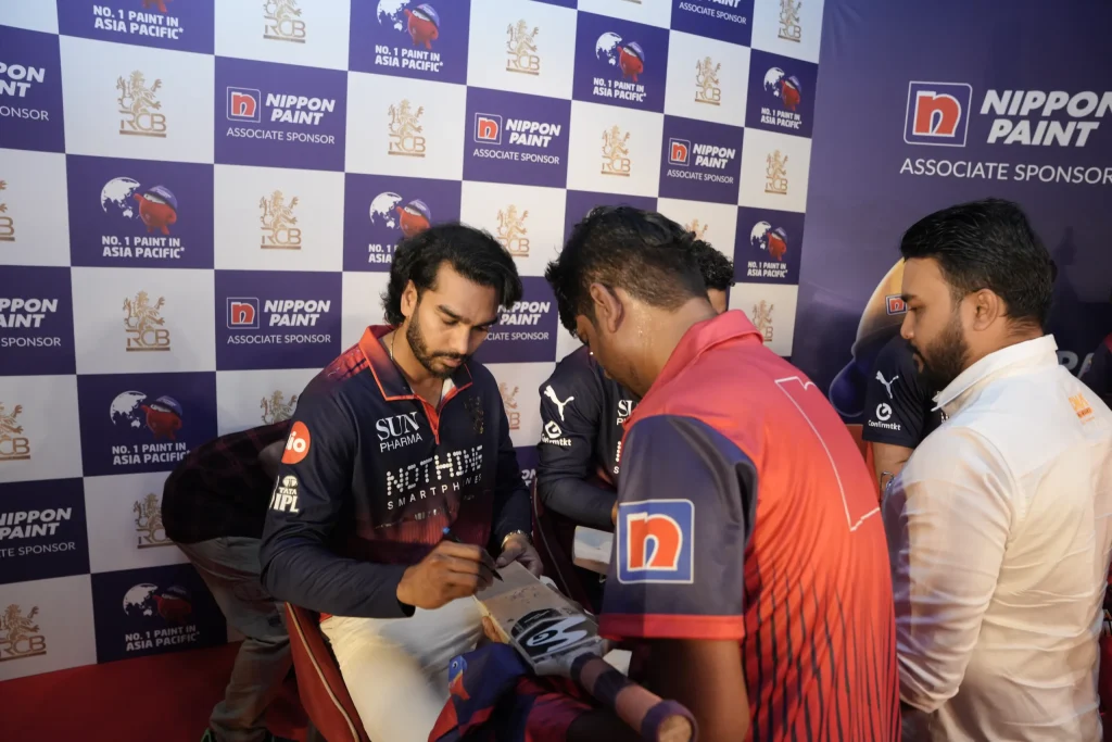 An RCB cricket player signs a miniature wooden bat for a fan.
