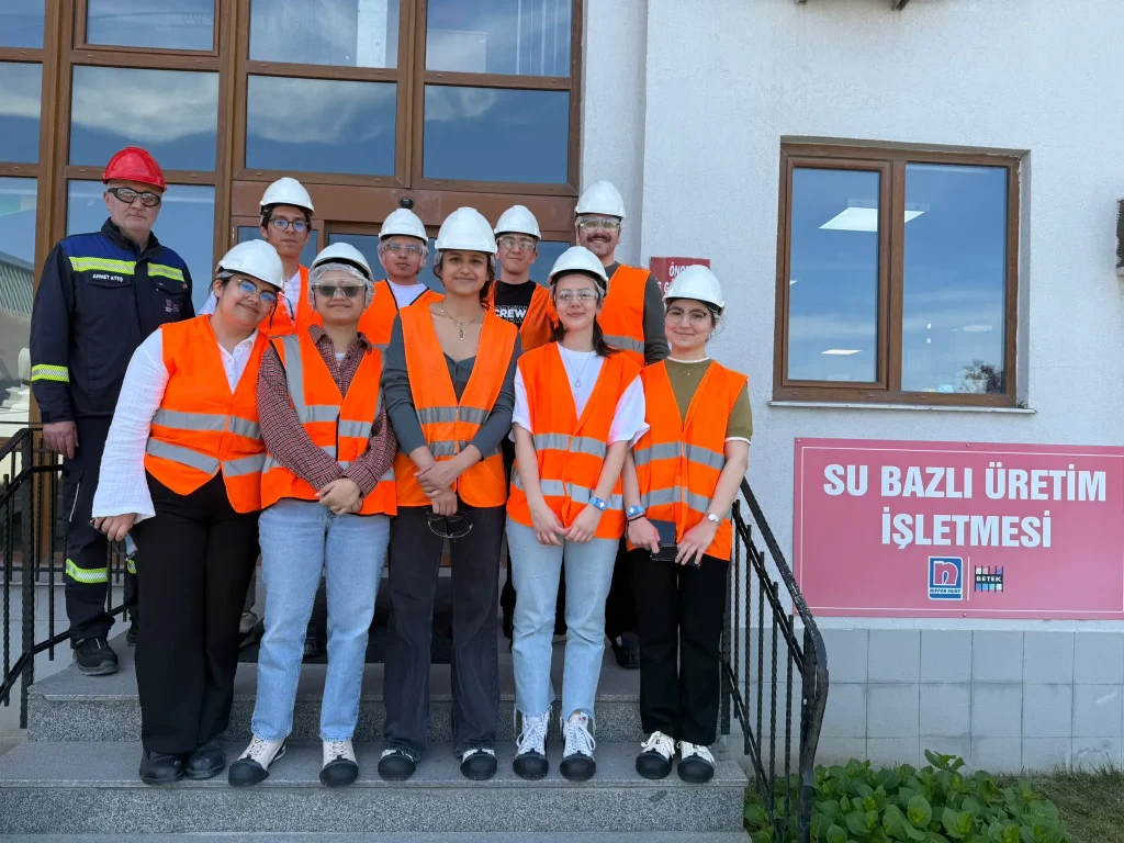 Engineering students wearing hard hats and safety vests stand outside a Betek production facility.