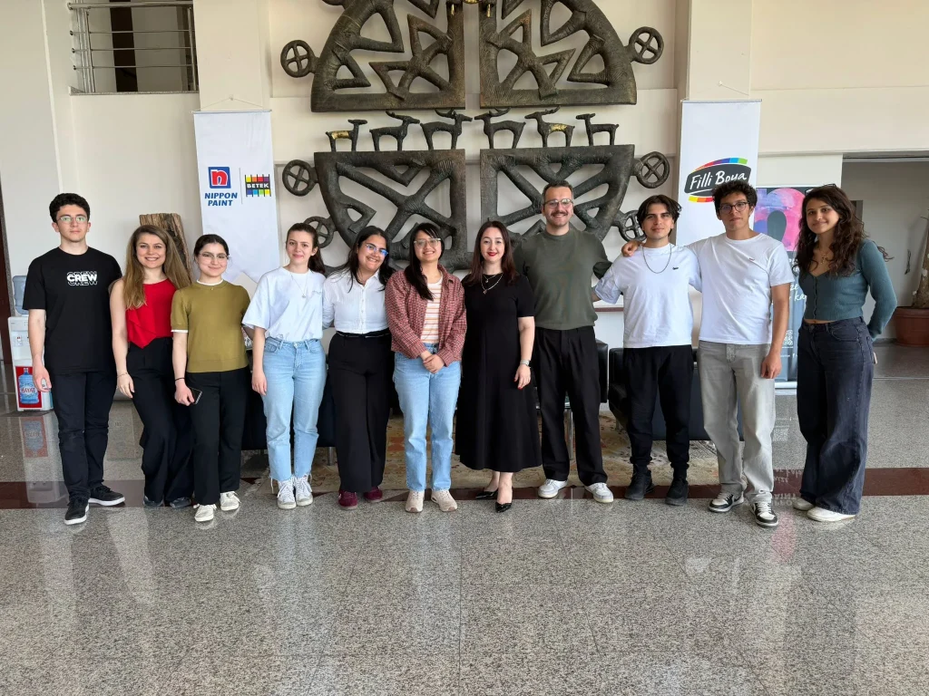 A group of university students and professionals pose in a lobby with corporate banners.