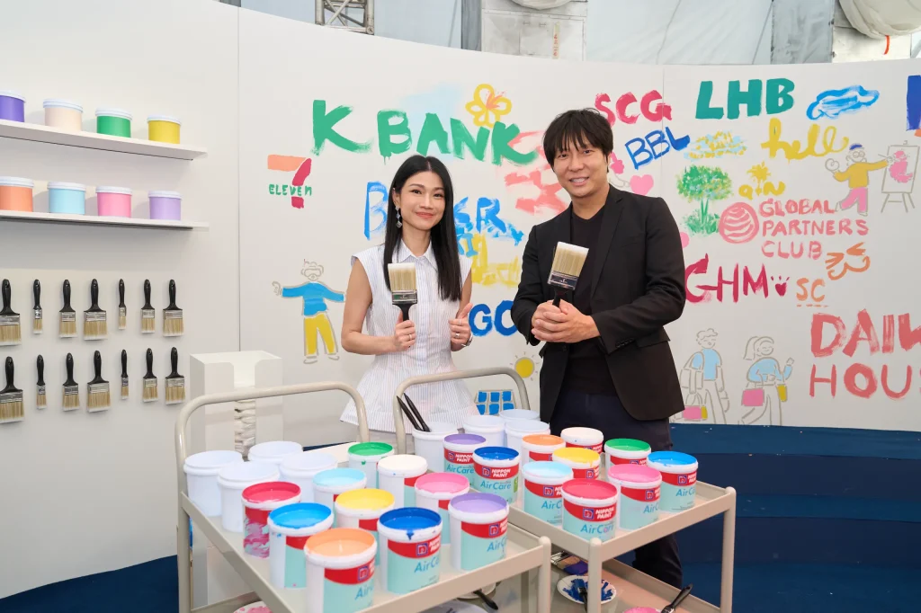 A man and woman smile while holding large paintbrushes at a colourful painting station.